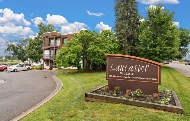 A sign for Lancaster Village is in the foreground of a grassy area.