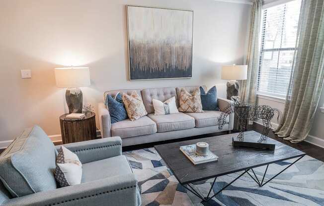 A living room with a grey couch, a grey armchair, a coffee table, and a painting on the wall.