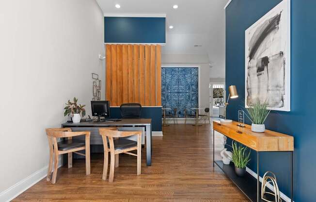 A room with a desk, chairs, and a blue wall.
