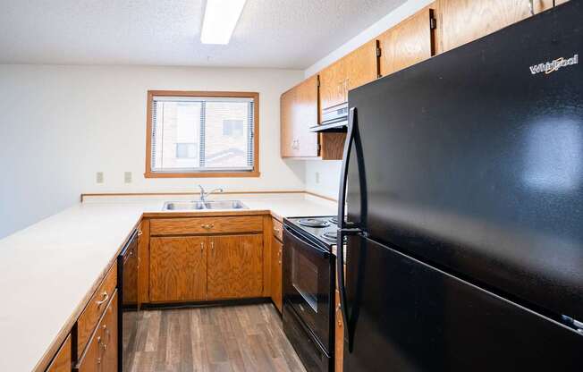 A black refrigerator is in the corner of a kitchen with wooden cabinets. Fargo, ND Westwood Estates