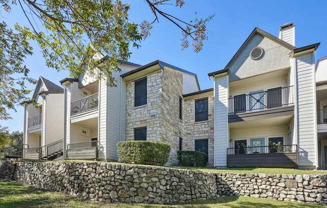 Our apartment buildings with balconies and a stone wall at On the Green apartments in Austin, TX