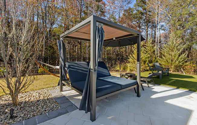 A grey and black outdoor daybed with a canopy is in the middle of a paved area.