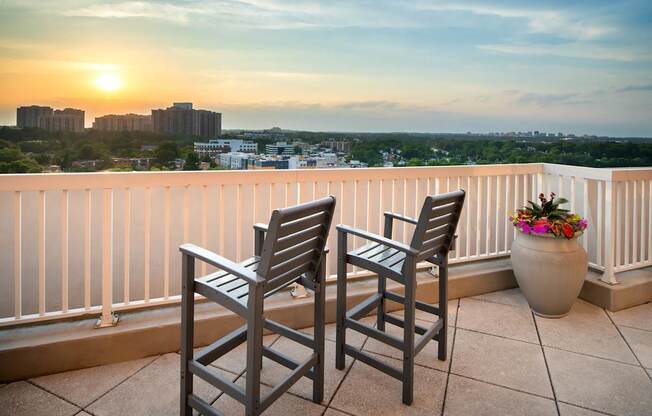 Two chairs are on a balcony with a sunset view.