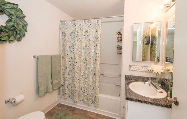 A bathroom with a floral shower curtain and a mirror above the sink at Bishop's Court Apartments, California, 95670