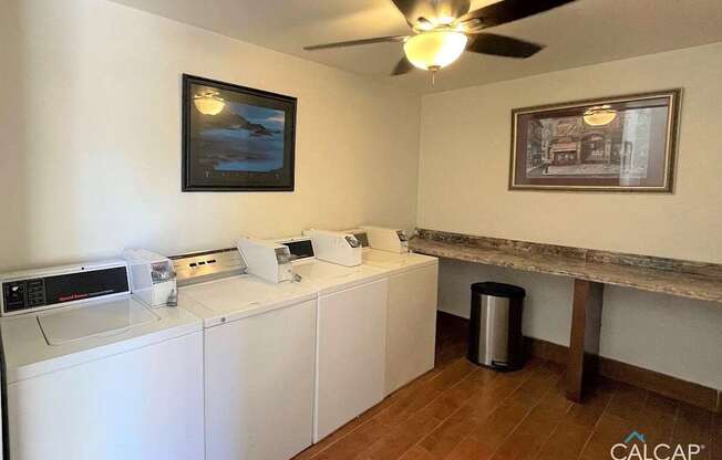 A laundry room with a washer and dryer, a trash can, and a ceiling fan.