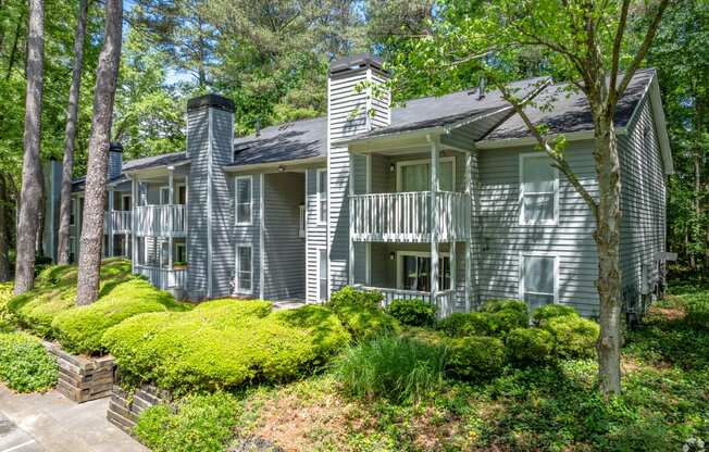 the view of a gray house with a deck and trees