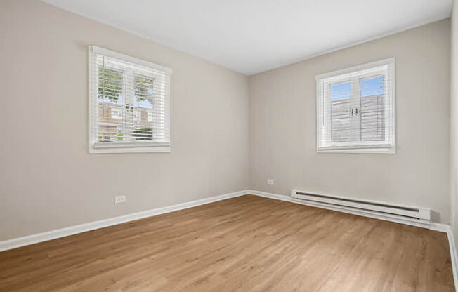 A bedroom with wooden floors and two windows.