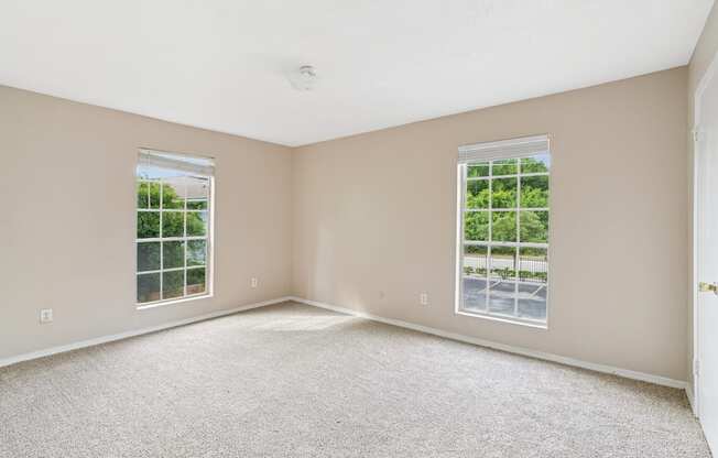 A room with carpeted floor and two windows.
