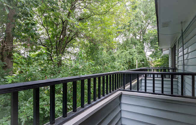 A balcony with a black railing overlooks a lush green forest.