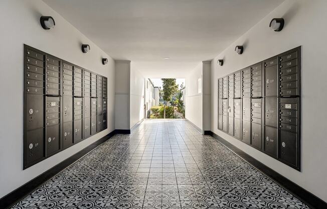 A long hallway with black and white tiles and a black wall with many mailboxes.