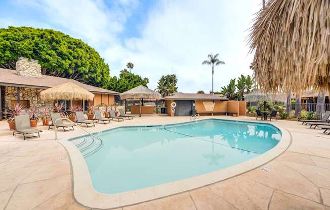 A large outdoor swimming pool surrounded by lounge chairs and thatched umbrellas.