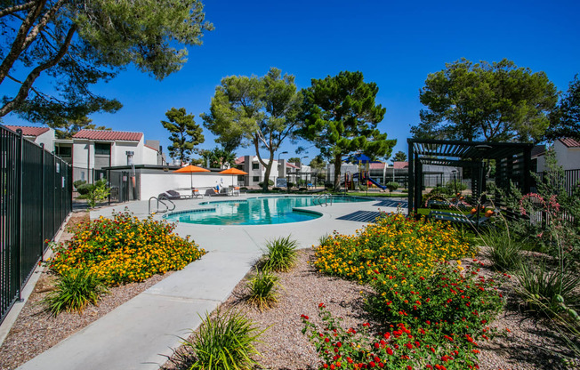 a pool is surrounded by flowers and trees and a fence