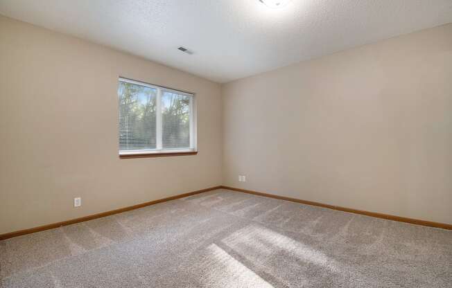 Omaha, NE Deerfield Apartments. An empty bedroom with a large window and beige walls