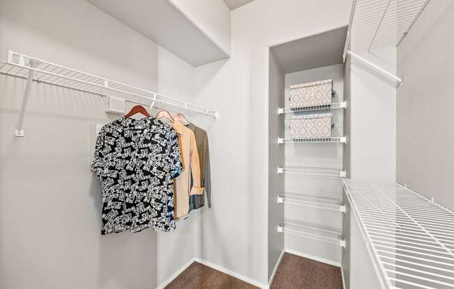 A white closet with clothes hanging and shelves.