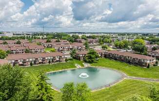 A large pond in the middle of a grassy area surrounded by houses.