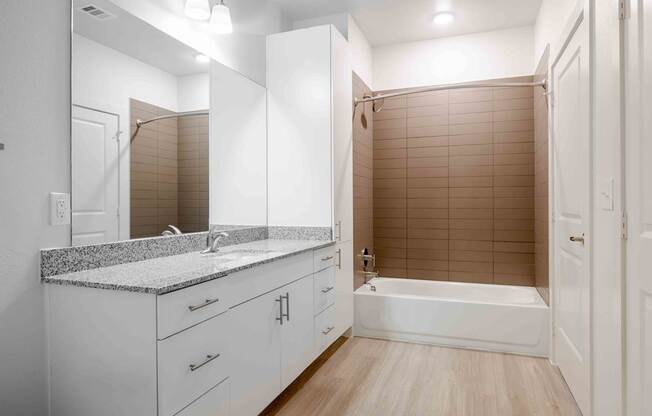 A white bathroom with a sink, mirror, and tub.