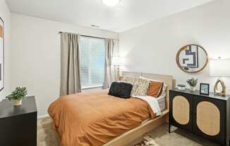 A bedroom with a bed, nightstand, and a round mirror on the wall.
