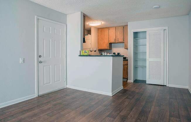 an empty living room with a kitchen and a door to a closet