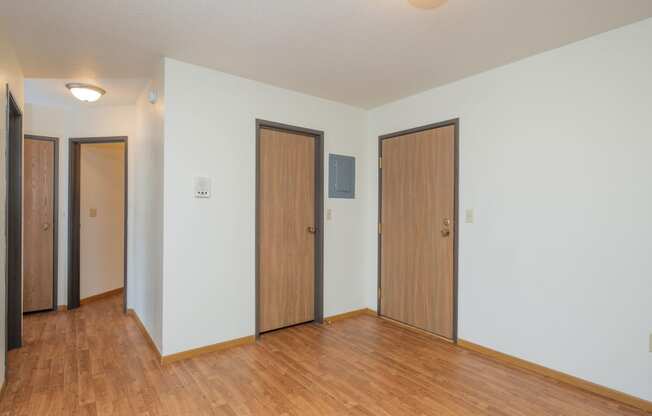 the living room of an empty apartment with wood flooring and three doors. Fargo, ND Park Circle Apartments.