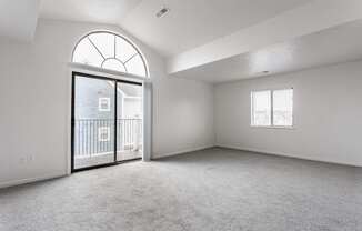 A spacious room with a large arched window and a sliding glass door leading to a balcony.