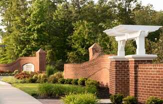 Community entrance with brick sign; road surrounded by trees