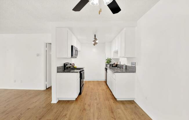 an empty kitchen with white walls and wood floors and a ceiling fan at Casa Del Amo Apartments, Torrance California