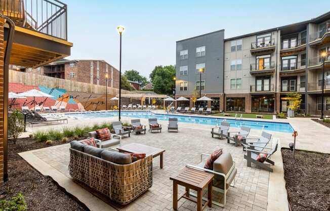 a swimming pool with lounge chairs and tables in front of an apartment building