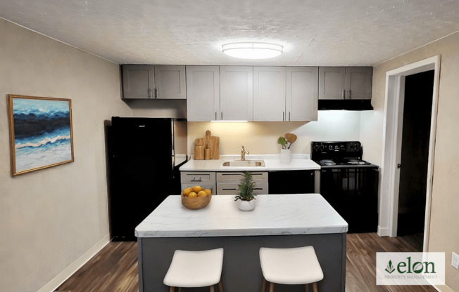 A kitchen with a black refrigerator, white cabinets, and a painting on the wall.