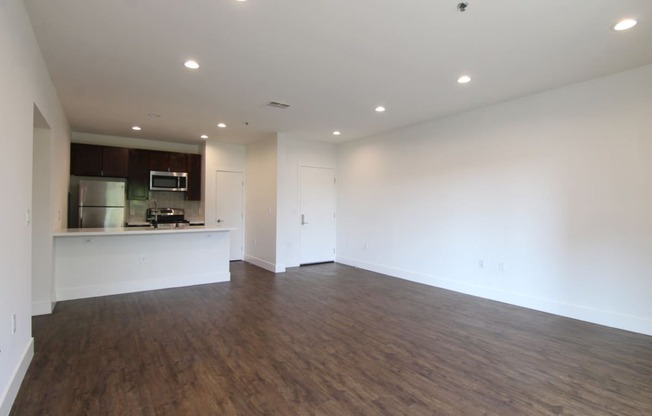 Hardwood floored living room with can lights and view of kitchen.