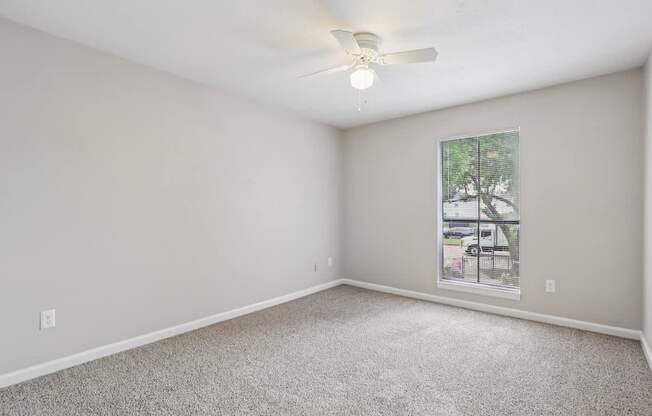 A room with a ceiling fan and a window showing a parking lot outside.