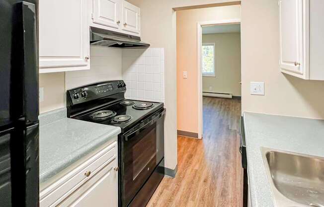 A kitchen with a black fridge, black stove, and white cabinets at The Hampton Meadows Apartments,Des Moines