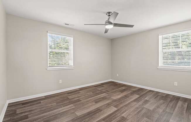 an empty room with a ceiling fan and two windows