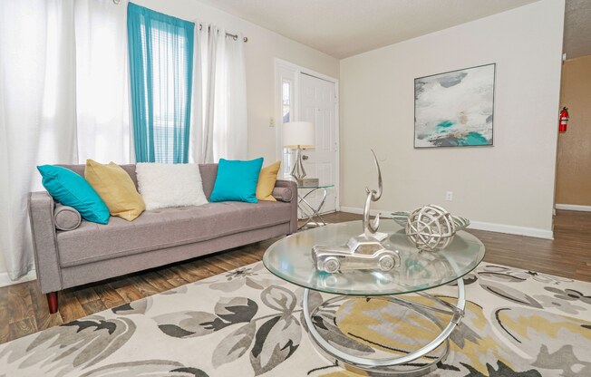 A living room with a grey couch and a glass coffee table at The Drake in Bossier City, LA