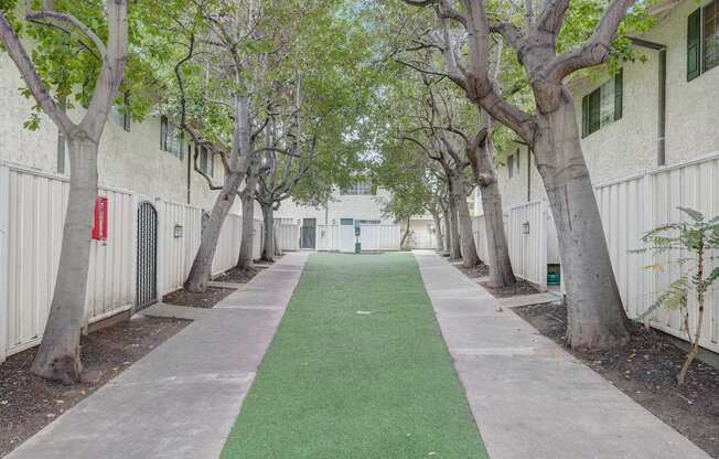a green walkway between two white buildings with trees