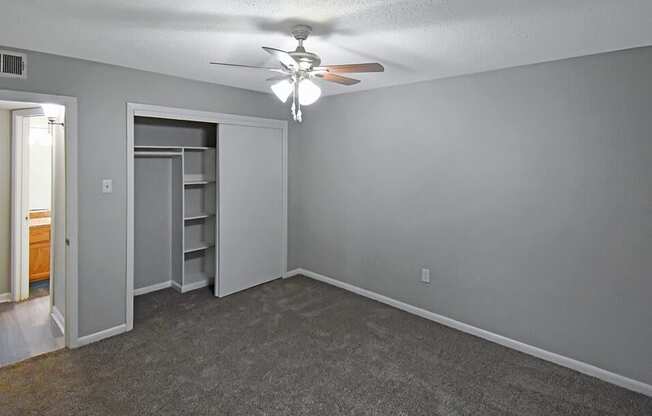 an empty living room with a ceiling fan and a closet