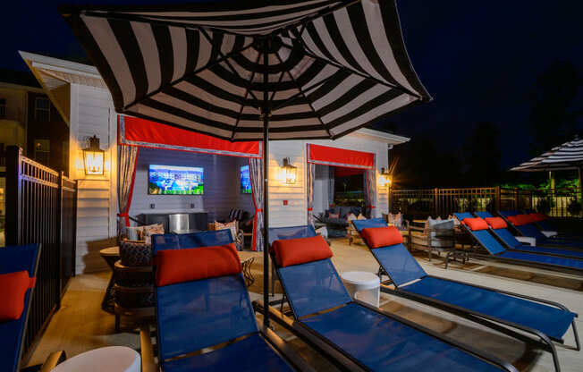 A row of lounge chairs are arranged in front of a building with a large screen and umbrella.