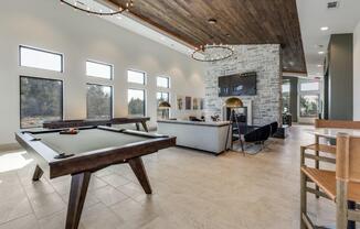 A pool table is in the middle of a room with a stone fireplace and a TV above it.