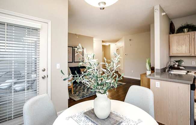 A dining room with a table and chairs and a vase of flowers.