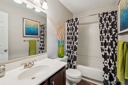 A bathroom with a white sink, toilet, and a painting on the wall.