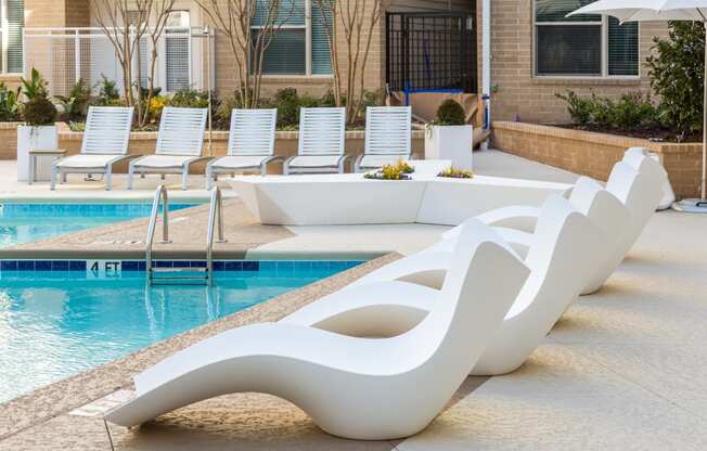 a row of white chaise lounges sit next to a swimming pool