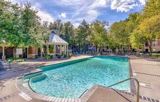 A large outdoor swimming pool surrounded by trees and a gazebo.