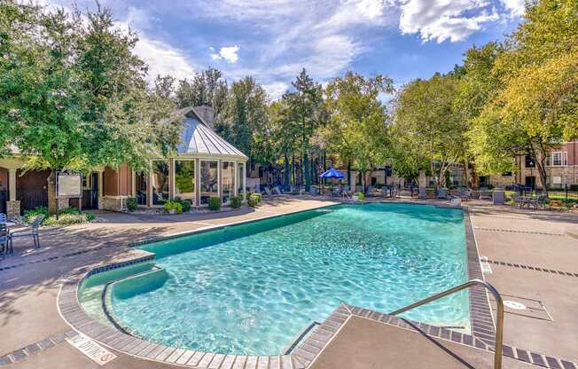 A large outdoor swimming pool surrounded by trees and a gazebo.