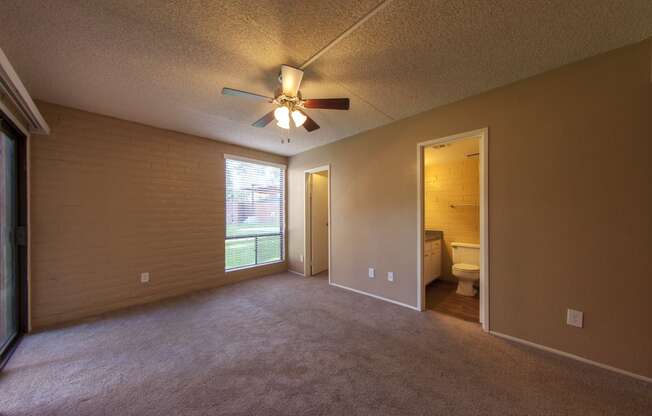 an empty living room with a ceiling fan and a door to a bathroom