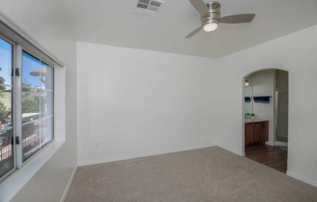 an empty living room with a large window and a ceiling fan