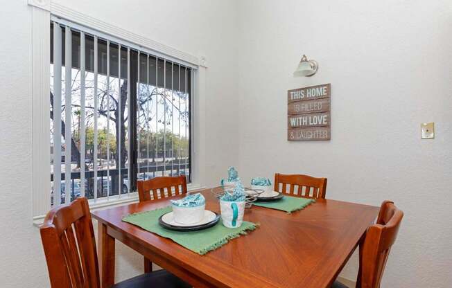 A dining table set with a green placemat and a sign on the wall that says "This home is filled with love and laughter".