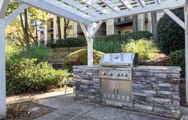 A BBQ grill is built into a stone wall under a white pergola.