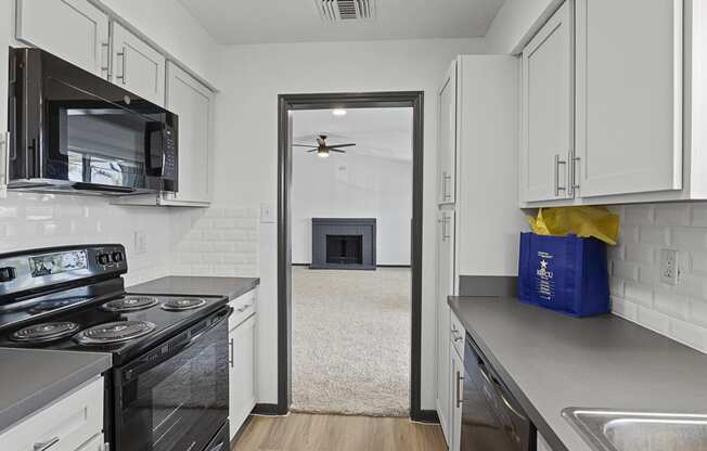 a kitchen with white cabinets and black appliances and a doorway to a living room