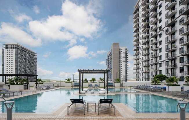 A pool area with a pergola and chairs in front of apartment buildings. at Palma, Doral, Florida