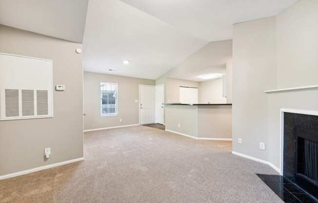 an empty living room with a fireplace and a kitchen