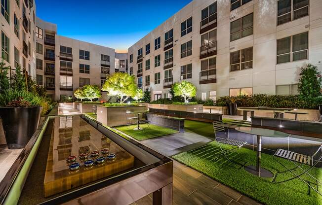 Courtyard game lounge with illuminated shuffleboard table, greenery, and intimate seating under the night sky